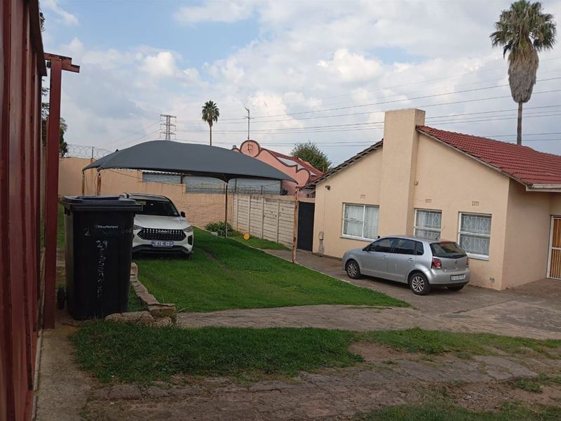 Rear exterior view of the property featuring a tiled roof, plastered walls, paved driveway, and a shade sail structure over the parking area.