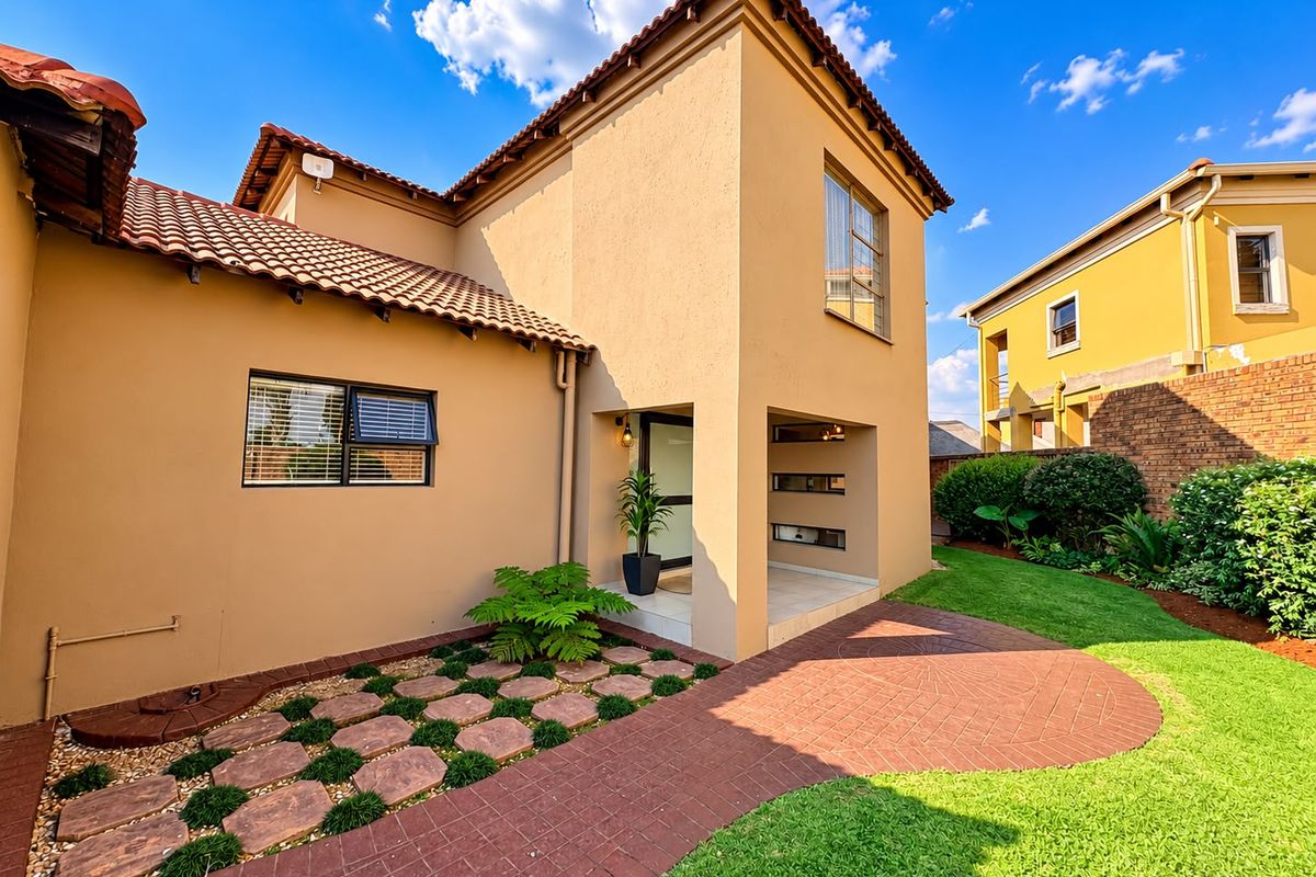 A well-maintained rear exterior view featuring a paved walkway, landscaped garden, and a covered entrance with terracotta roof tiles.