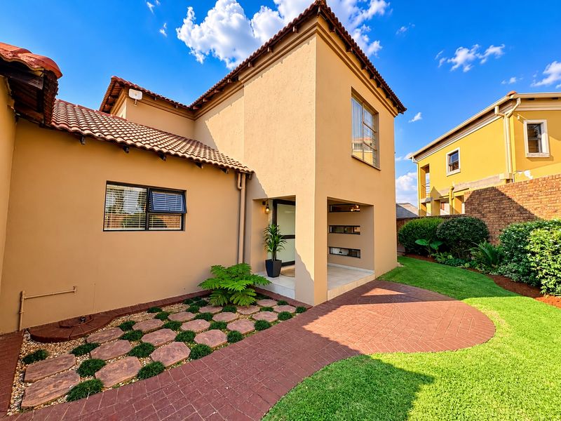 A well-maintained rear exterior view featuring a paved walkway, landscaped garden, and a covered entrance with terracotta roof tiles.