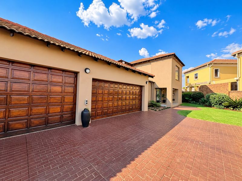 Front elevation of a well-maintained house featuring a double garage with wooden doors, a paved driveway, and a neat garden area.