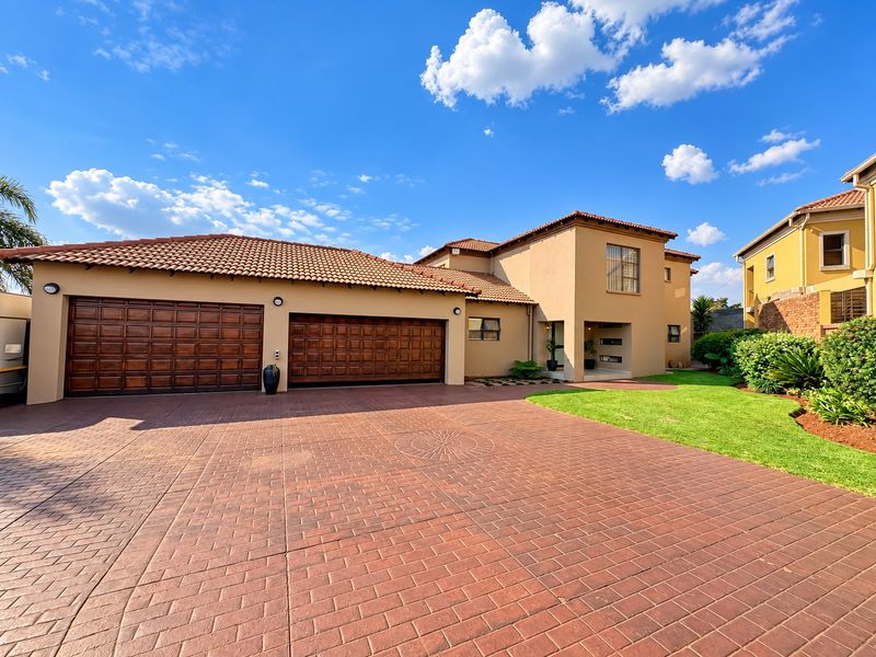 A well-maintained double-story house featuring a spacious paved driveway, double garage, and neat landscaped garden under a clear blue sky.