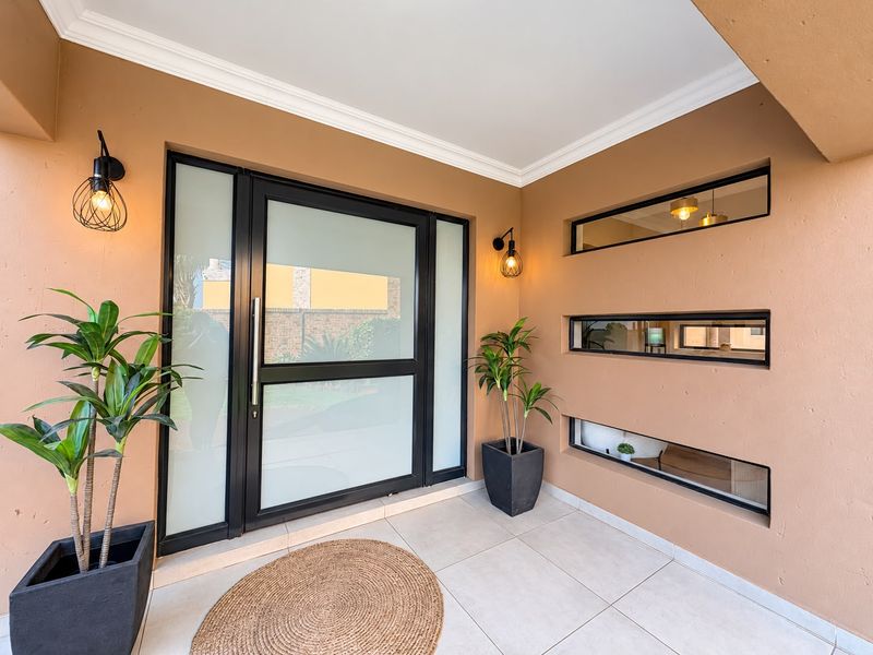 A modern, well-maintained entrance featuring a sleek black-framed frosted glass door, horizontal feature windows, and contemporary wall lighting.