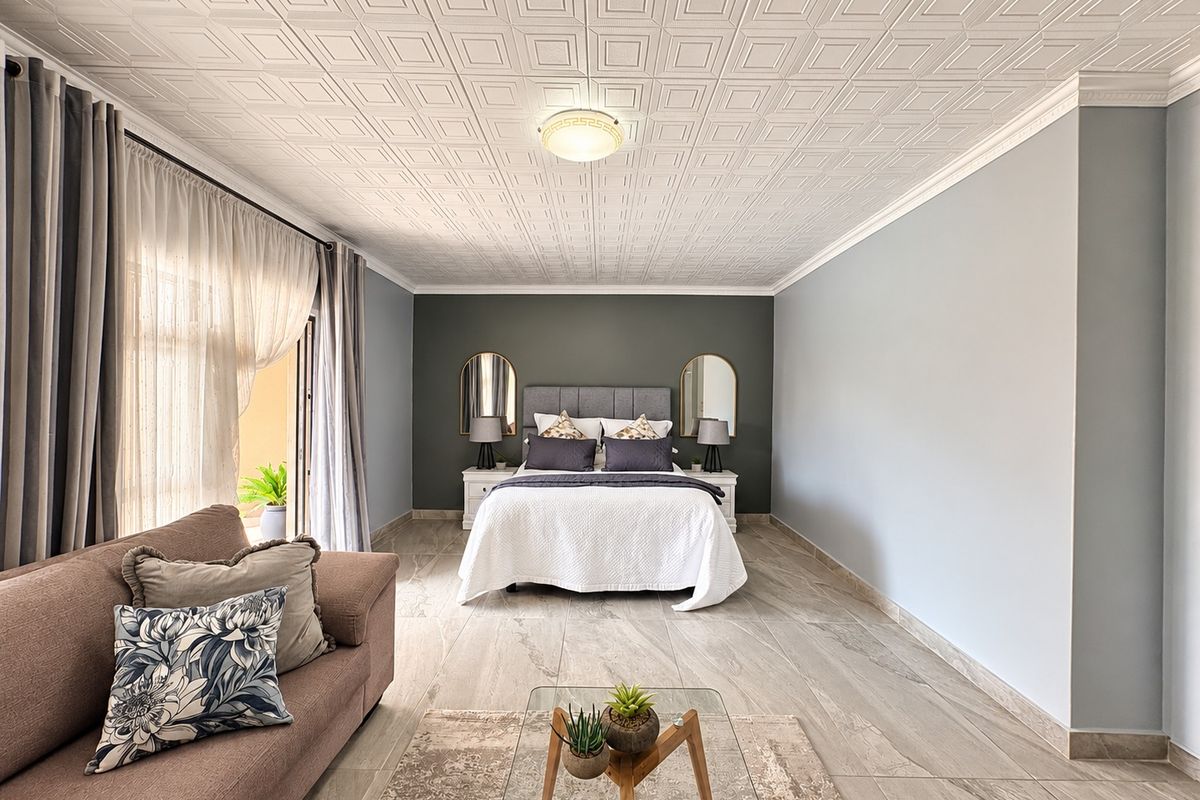 Spacious bedroom featuring tiled flooring, decorative ceiling tiles, crown molding, and direct access to an outdoor area through sliding glass doors.