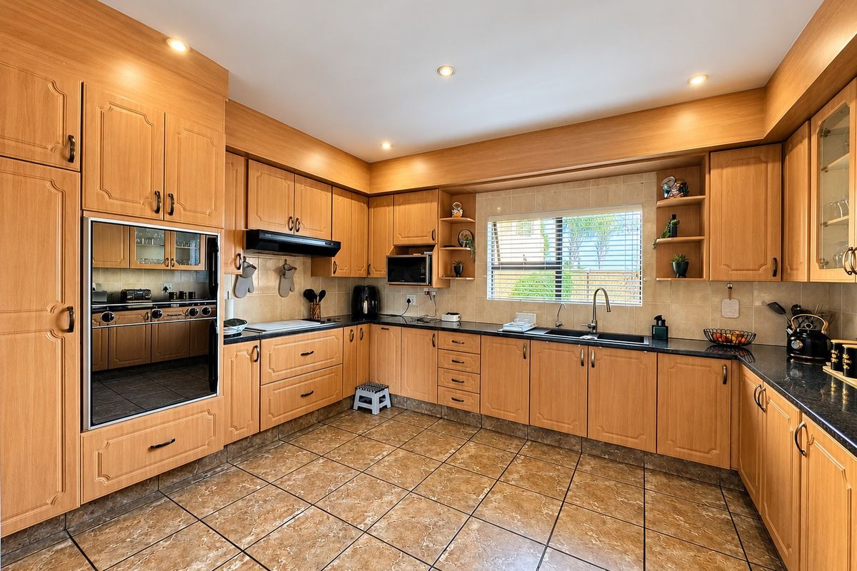 A functional kitchen featuring extensive wooden cabinetry, integrated oven, built-in microwave, double sink, and tiled flooring with a neutral backsplash.