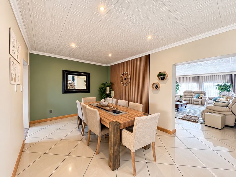 A well-maintained dining room featuring tiled floors, a decorative coffered ceiling, and a modern timber slat feature wall, flowing into the adjacent living area.