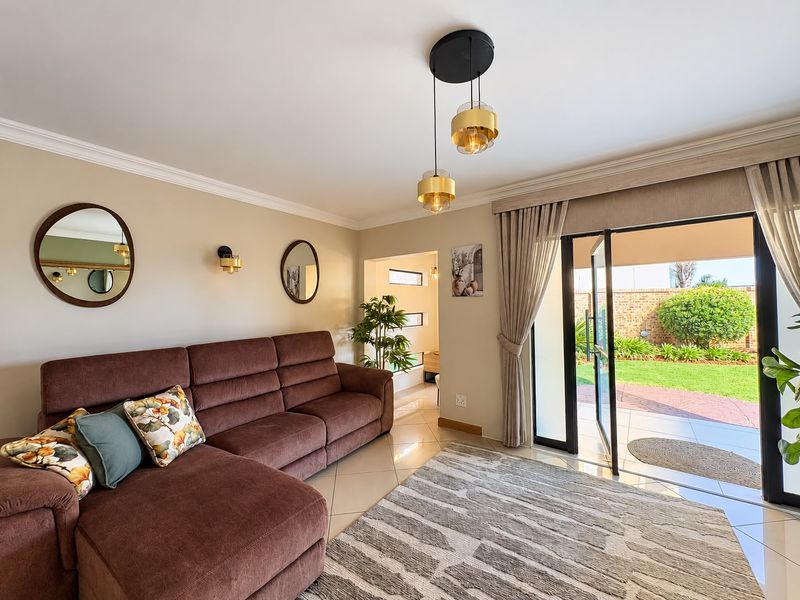 A well-maintained living room featuring tiled floors, modern pendant lighting, and a large sliding glass door providing direct access to the rear garden.