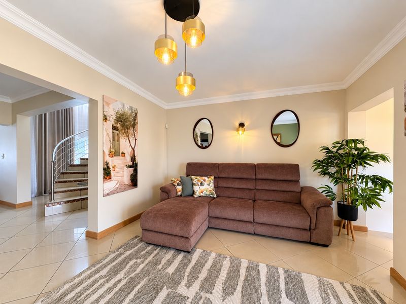 A well-maintained living room featuring tiled flooring, crown molding, and elegant pendant lighting, with an adjacent staircase visible in the background.