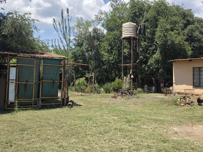 Rear exterior view of the small holding featuring a water storage tank, metal outbuilding structures, and a main dwelling with a corrugated roof.