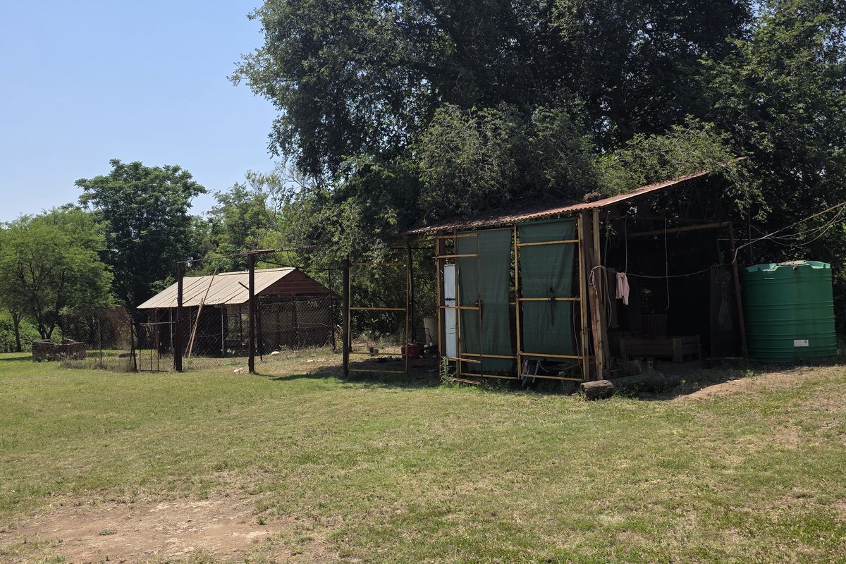 Expansive garden area featuring mature trees, basic metal outbuildings, and a water storage tank on a small holding property.