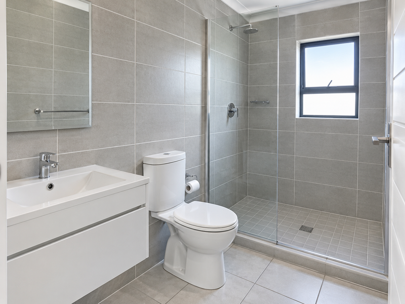 Modern bathroom featuring a wall-mounted vanity, walk-in shower with glass screen, and neutral grey tiling throughout.