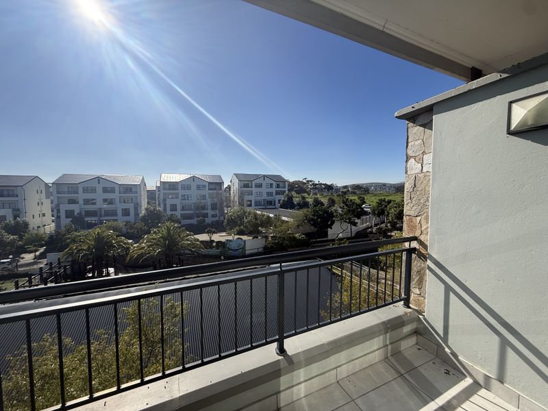 A clean, well-maintained balcony featuring tiled flooring, a metal balustrade, and stone cladding, offering an open view of the surrounding residential complex.