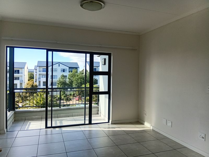 An empty, well-lit living area featuring neutral tiled flooring and a large sliding glass door that opens onto a private balcony.