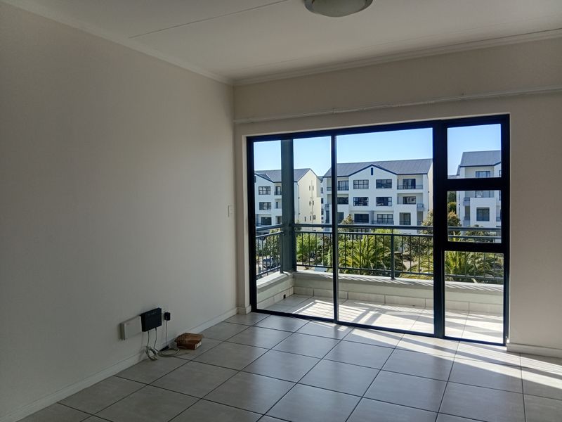 A bright, empty living area featuring neutral tiled flooring and large sliding glass doors that open onto a private balcony with neighborhood views.