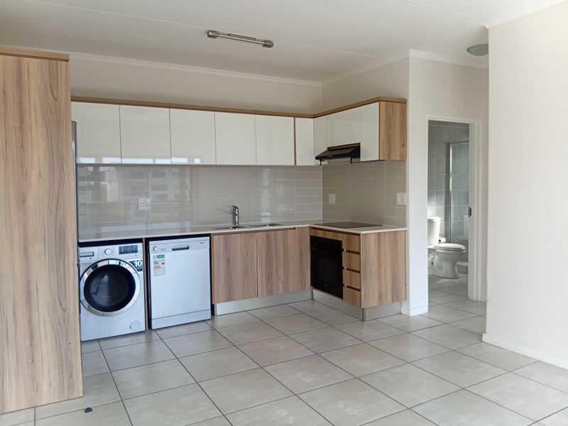 Modern open-plan kitchen featuring light wood-grain cabinetry, white upper cabinets, subway tile backsplash, and integrated appliances, with tiled flooring throughout.