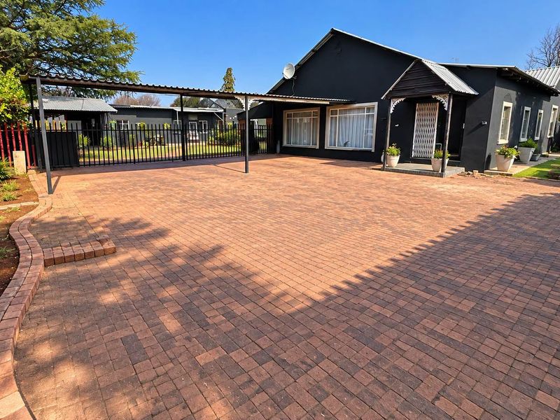 Spacious front exterior featuring a large paved driveway, covered carport, and well-maintained garden beds with brick edging.
