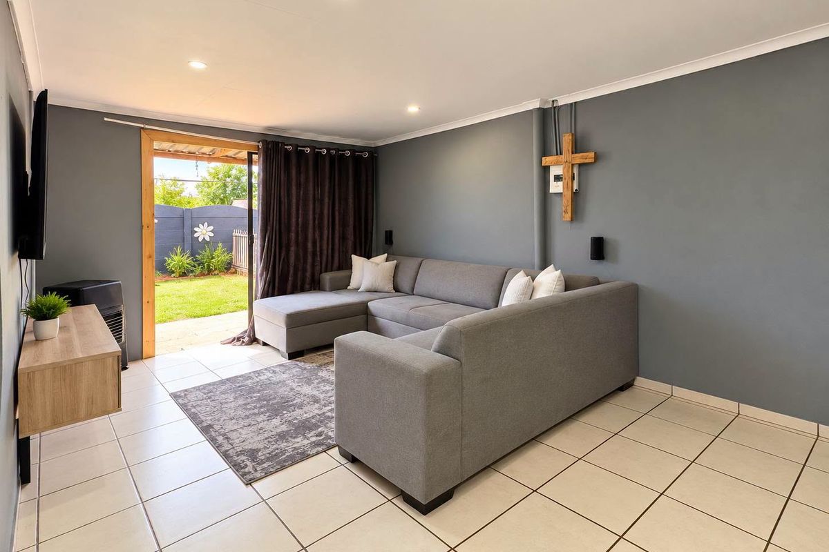 A well-maintained living room featuring neutral ceramic floor tiles, recessed lighting, and a sliding glass door providing direct access to the rear garden.