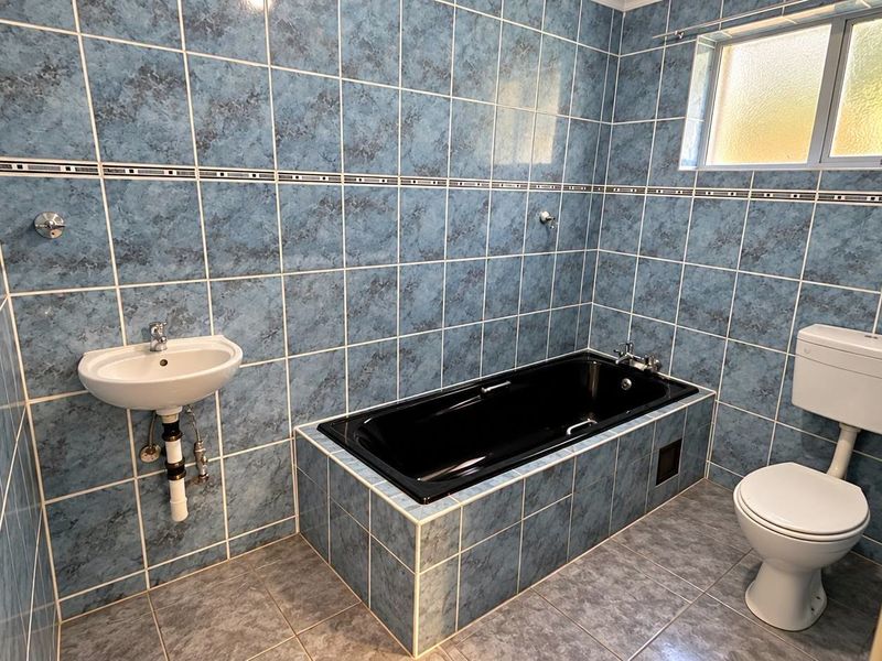 A dated bathroom featuring blue tiled walls, a black built-in bathtub, a wall-mounted basin, and a standard toilet.