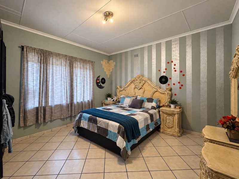 A spacious bedroom featuring tiled flooring, a feature wall with striped wallpaper, and large windows with curtain tracks.