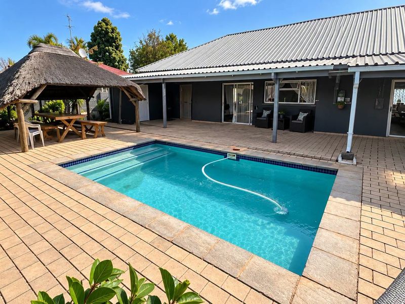 Outdoor entertainment area featuring a swimming pool, paved patio, and a thatched lapa, perfect for relaxation and hosting guests.