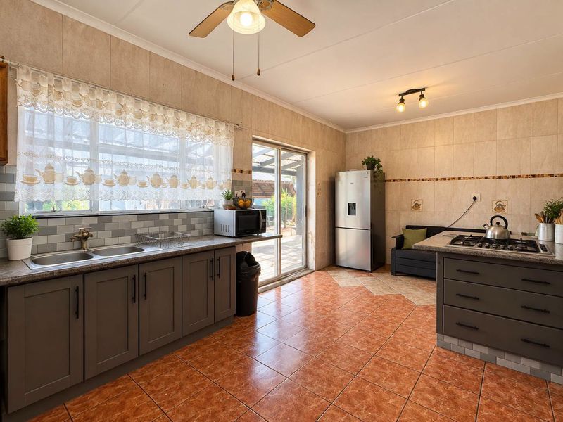 Spacious kitchen featuring dark grey cabinetry, tiled flooring, a gas hob, and direct access to the outdoor area through a sliding glass door.