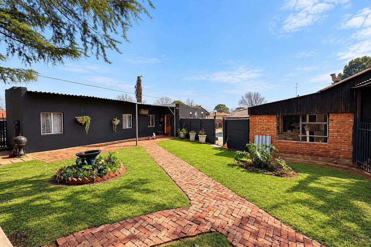 A spacious rear garden featuring a brick-paved pathway, well-maintained lawn, and a combination of painted masonry and exposed brick exterior walls.