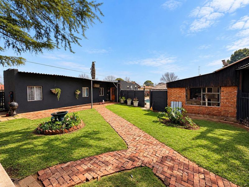 A spacious rear garden featuring a brick-paved pathway, well-maintained lawn, and a combination of painted masonry and exposed brick exterior walls.