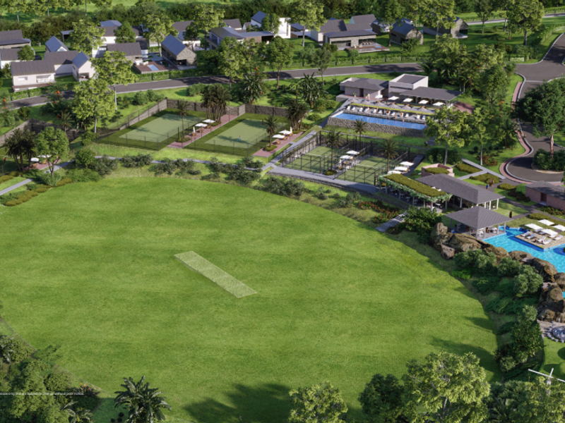 Aerial view of a residential estate featuring a cricket pitch, tennis courts, swimming pool, and clubhouse facilities within a landscaped environment.