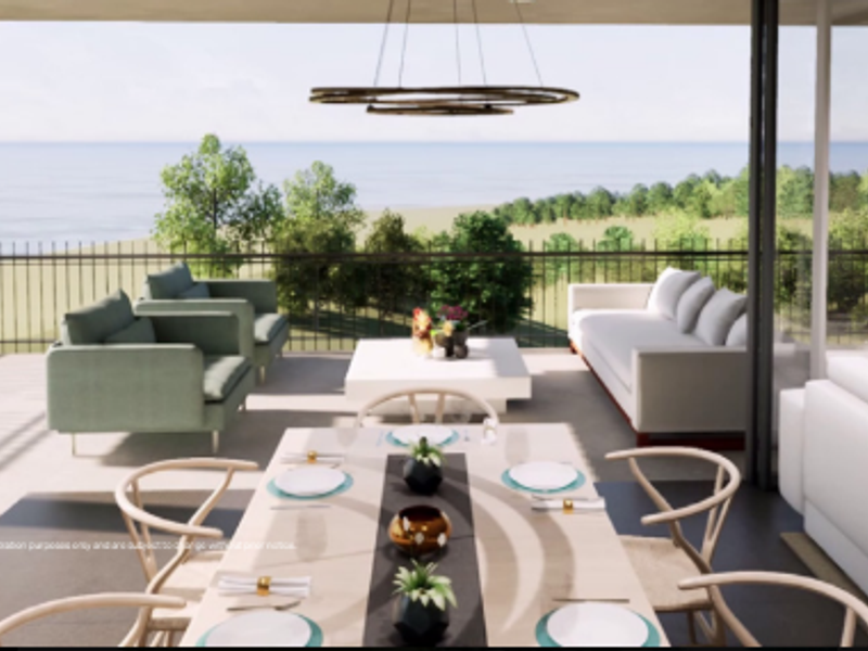 Spacious covered balcony featuring a modern metal railing and expansive ocean views, seamlessly connected to the interior living space through large sliding glass doors.