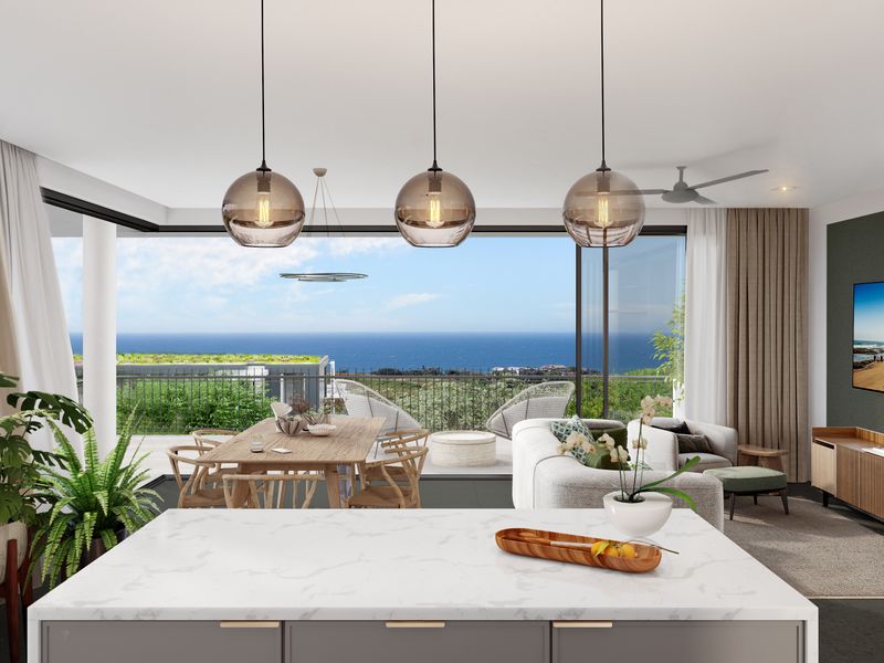 Modern open-plan living area featuring a sleek kitchen island, contemporary pendant lighting, and expansive sliding doors opening to a scenic ocean view balcony.