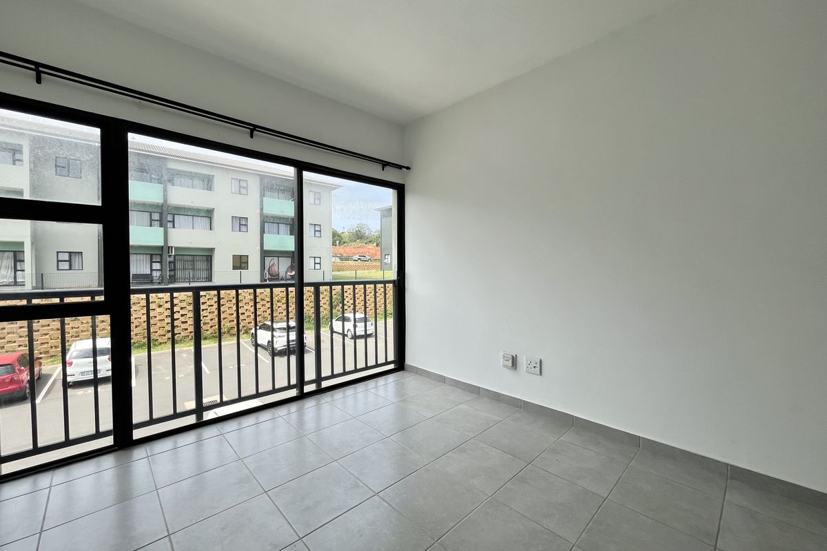 A bright, empty living area featuring large sliding glass doors, neutral tiled flooring, and clean white walls, offering a modern and versatile space.