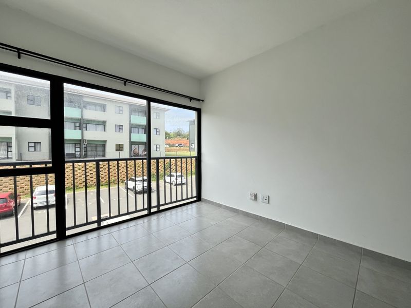 A bright, empty living area featuring large sliding glass doors, neutral tiled flooring, and clean white walls, offering a modern and versatile space.