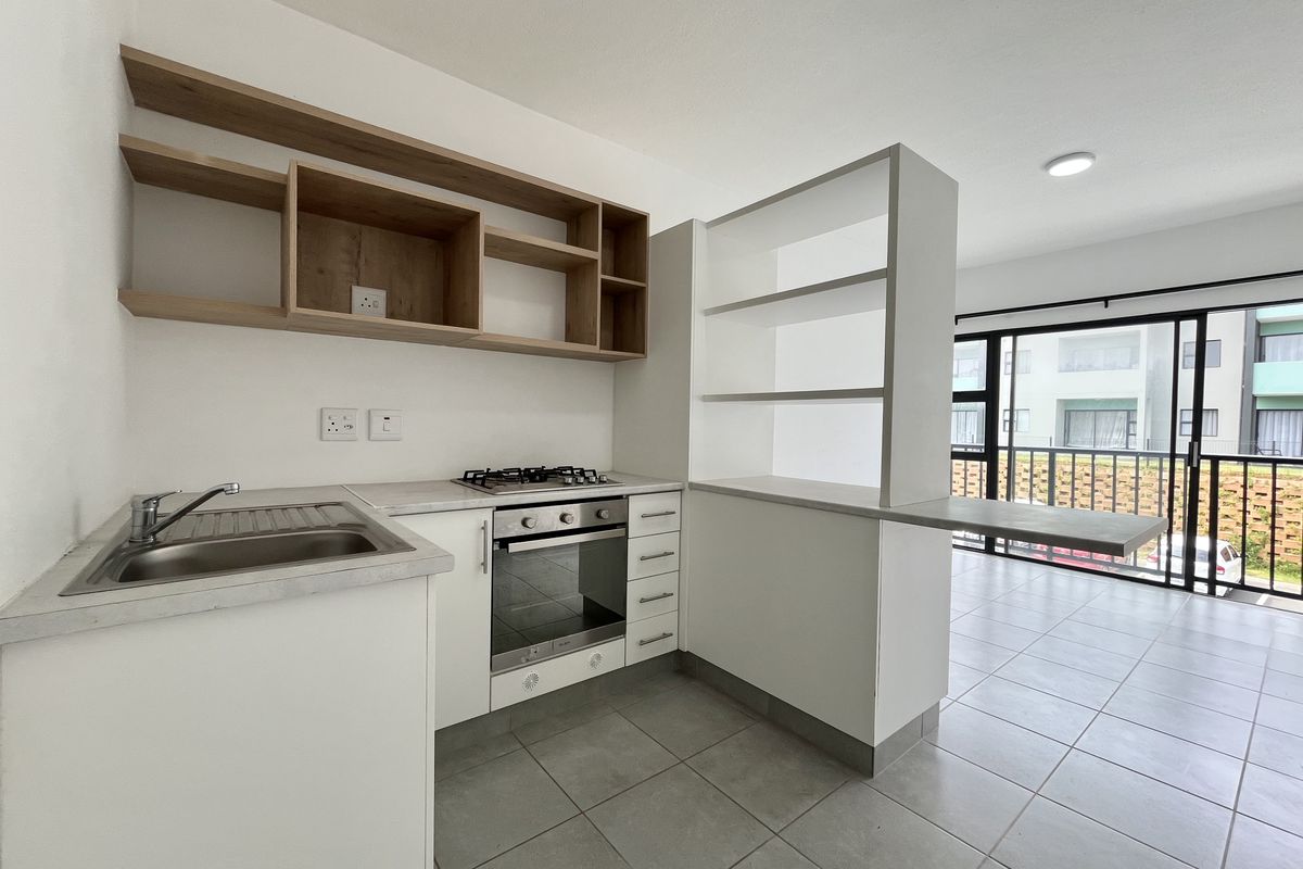 Modern open-plan kitchen featuring built-in oven, gas hob, stainless steel sink, and ample shelving, seamlessly connecting to a bright living area with sliding doors.