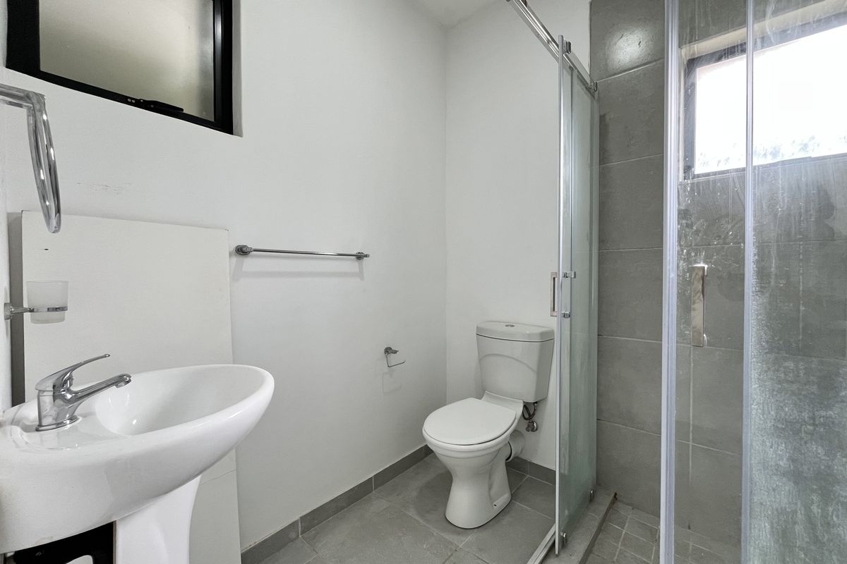 A functional bathroom featuring a pedestal sink, toilet, and a glass-enclosed shower with grey tiled flooring and wall accents.