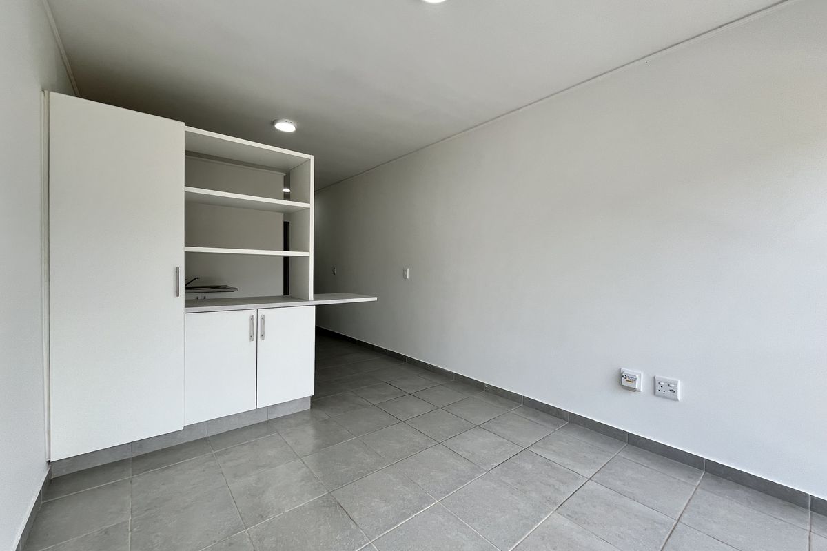 A clean, empty kitchen area featuring modern grey floor tiles, white built-in cabinetry with open shelving, and neutral wall finishes.