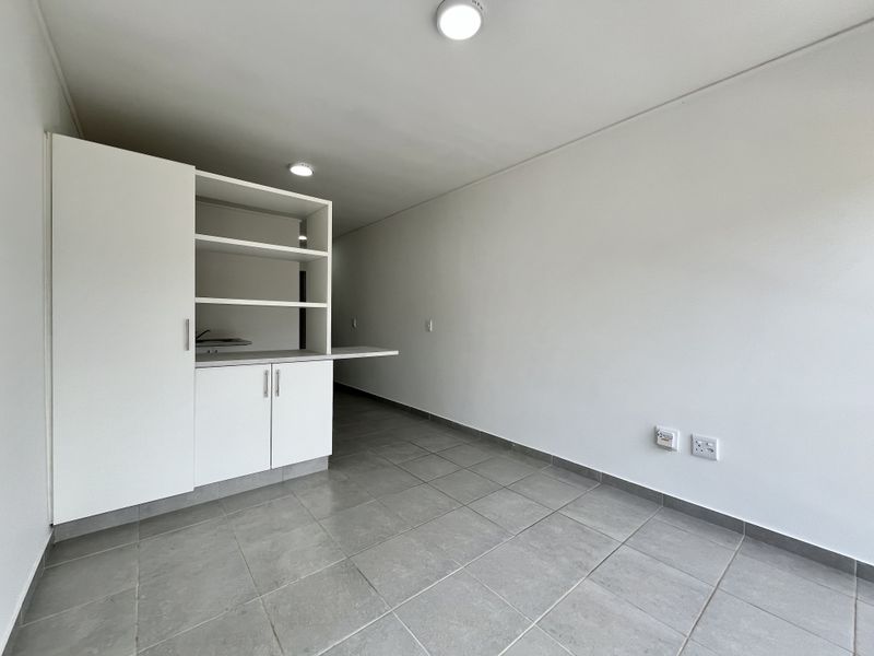A clean, empty kitchen area featuring modern grey floor tiles, white built-in cabinetry with open shelving, and neutral wall finishes.