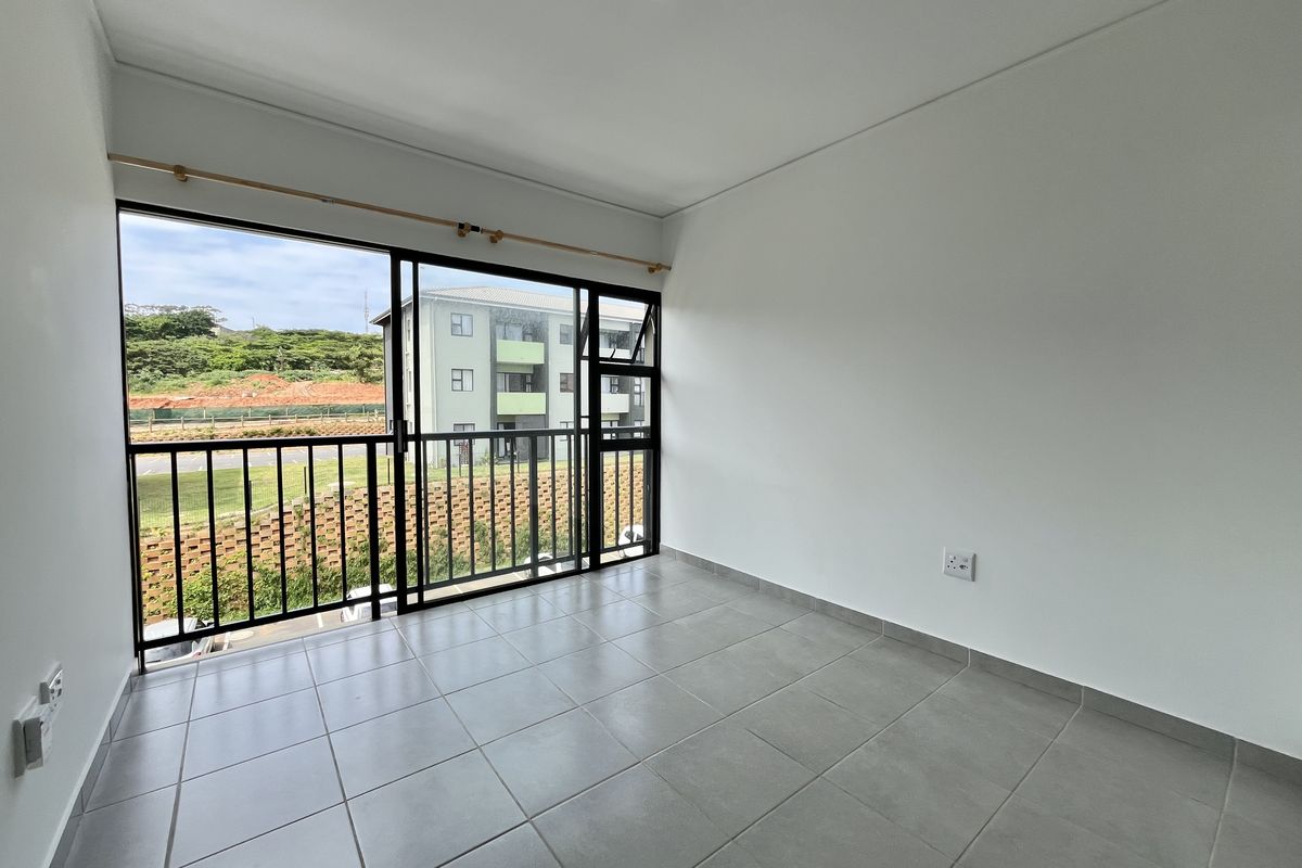 A bright, empty bedroom featuring neutral tiled flooring, a large sliding glass door leading to a balcony, and clean white walls.