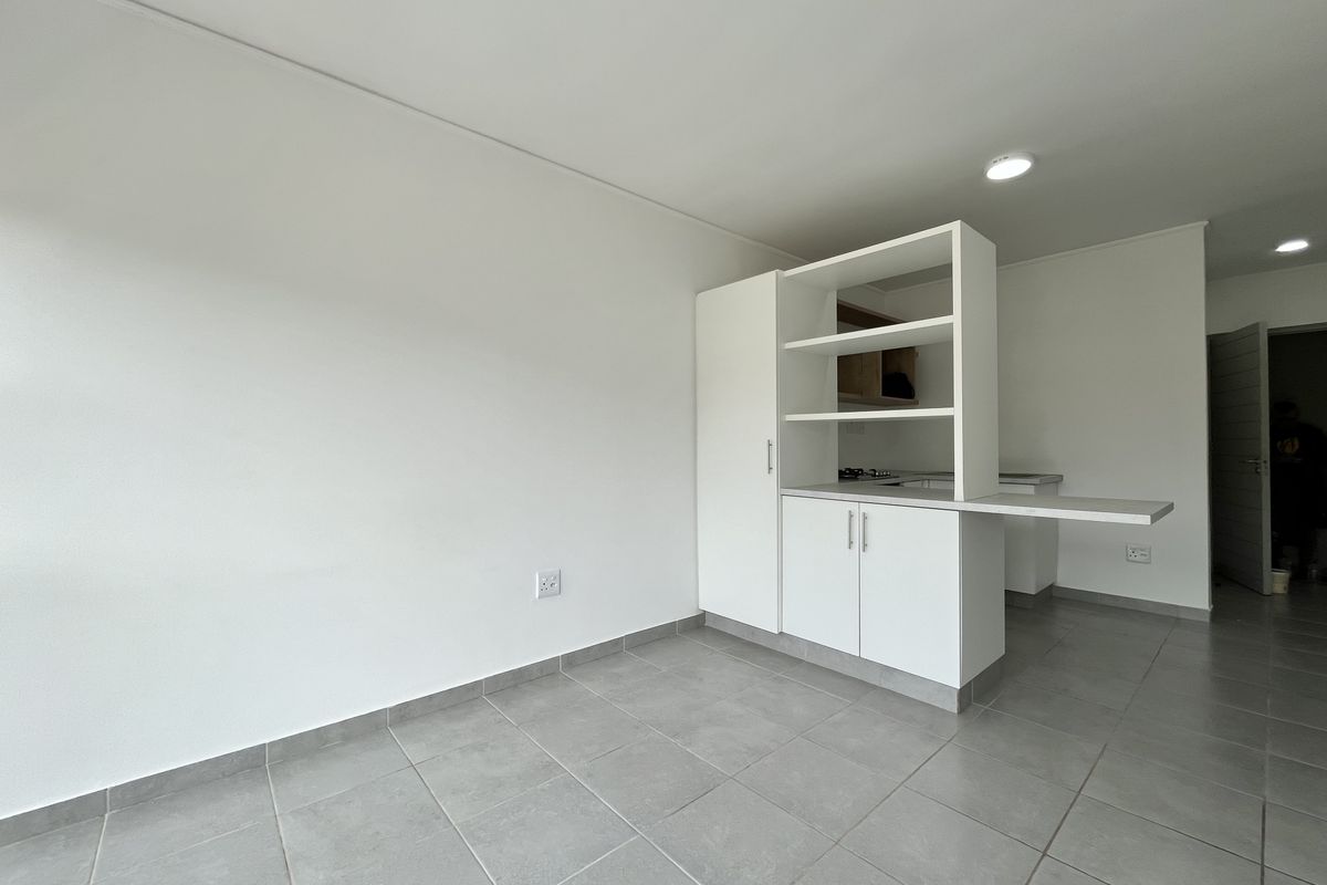 A bright, open-plan living and kitchen area featuring modern white cabinetry, a breakfast counter, and neutral tiled flooring throughout.