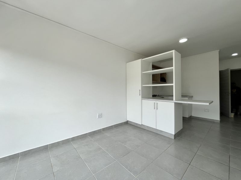 A bright, open-plan living and kitchen area featuring modern white cabinetry, a breakfast counter, and neutral tiled flooring throughout.