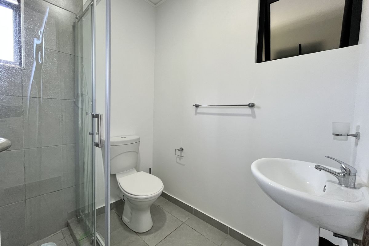 A clean and functional bathroom featuring a glass shower enclosure, pedestal basin, and modern tiled finishes.