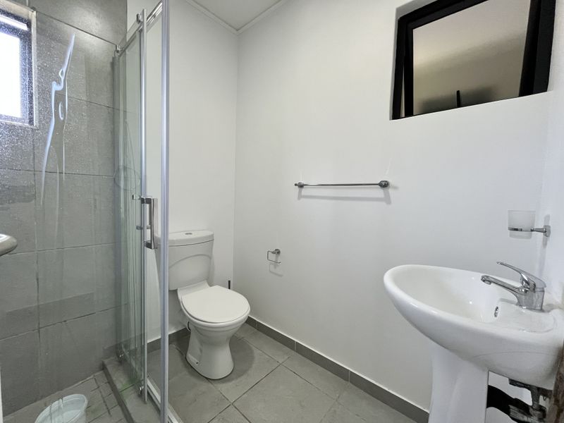 A clean and functional bathroom featuring a glass shower enclosure, pedestal basin, and modern tiled finishes.