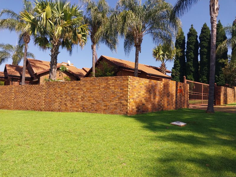 A well-maintained residential property featuring a classic face brick boundary wall, tiled roof architecture, and a secure metal driveway gate set within a lawned garden.