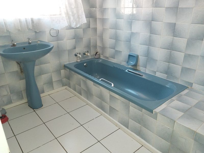 A dated bathroom featuring blue sanitaryware, including a pedestal basin and built-in bathtub, complemented by light blue wall tiles and white floor tiles.