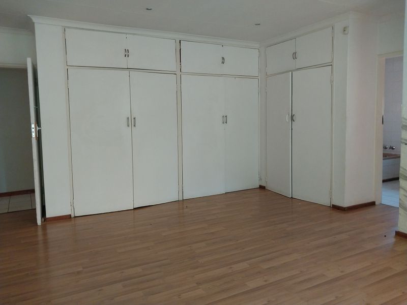 A spacious, empty bedroom featuring extensive built-in cupboard storage, laminate flooring, and recessed ceiling lighting.