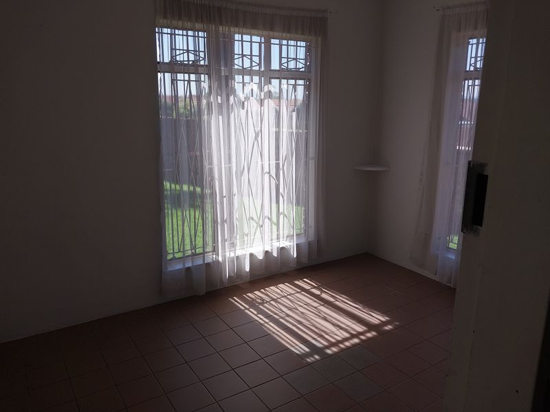 A vacant bedroom featuring tiled flooring, large windows with security bars, and a built-in corner shelf, offering a bright and functional space.