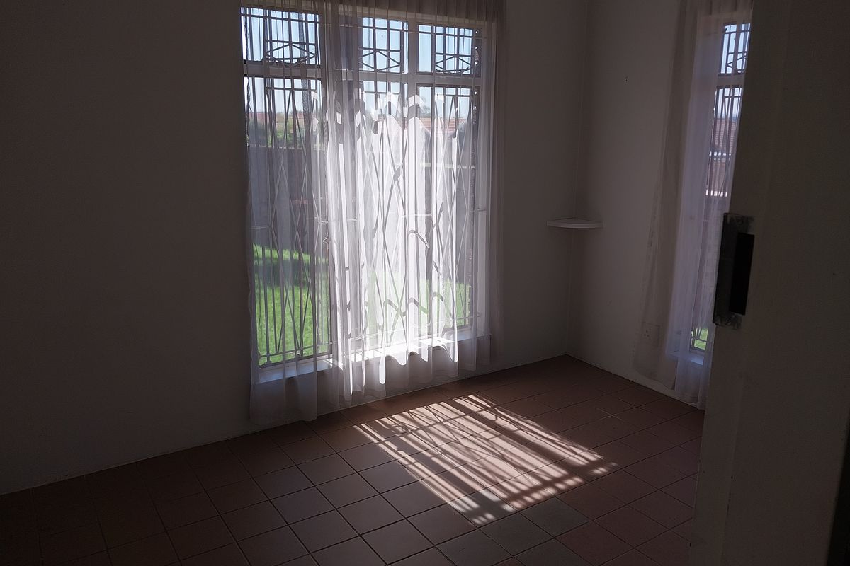 A vacant bedroom featuring tiled flooring, large windows with security bars, and a built-in corner shelf, offering a bright and functional space.