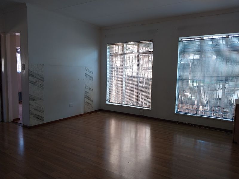 An empty living room featuring laminate flooring, large windows with venetian blinds, and security bars, offering a blank canvas for interior design.