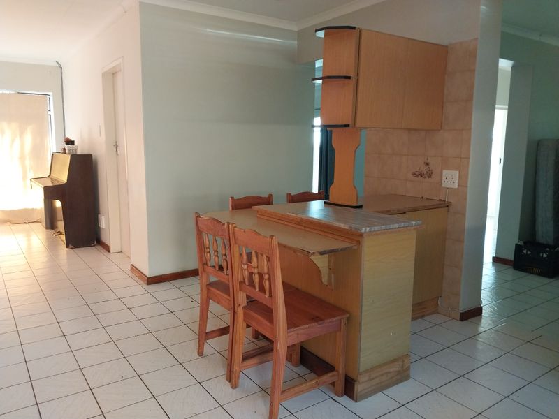 Open plan living area featuring tiled flooring and a dated built-in breakfast bar with integrated kitchen cabinetry.