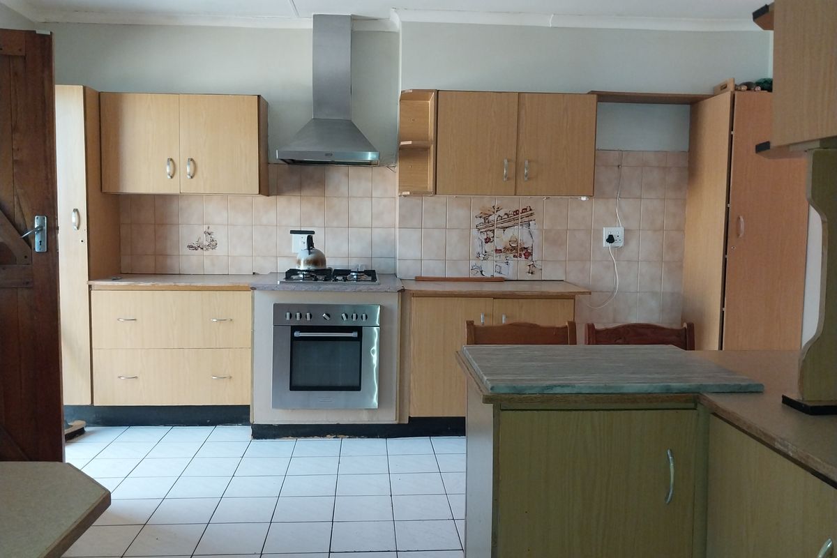 A functional kitchen featuring light wood cabinetry, a stainless steel oven and hob, tiled splashbacks, and white floor tiles.