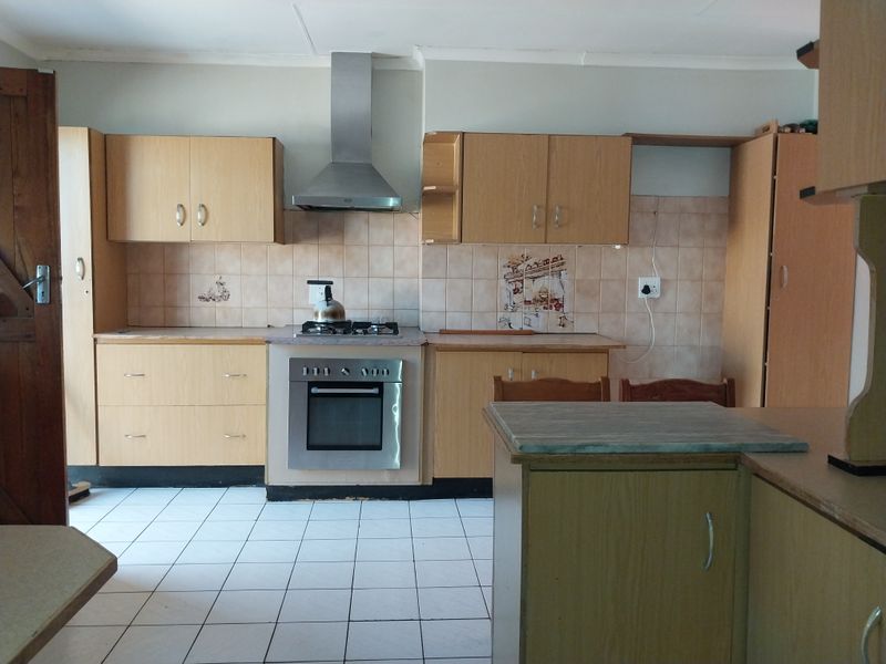 A functional kitchen featuring light wood cabinetry, a stainless steel oven and hob, tiled splashbacks, and white floor tiles.