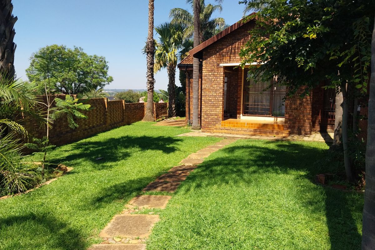 A well-maintained rear garden featuring a face brick house exterior, a paved patio area, and a stone pathway leading through the lawn.